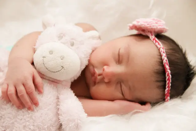 A baby sleeping holding a fluffy animal